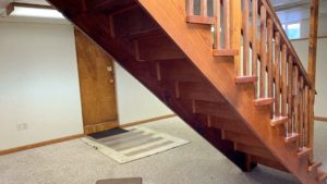 Basement den with carpet and wooden stairwell in the middle of the room