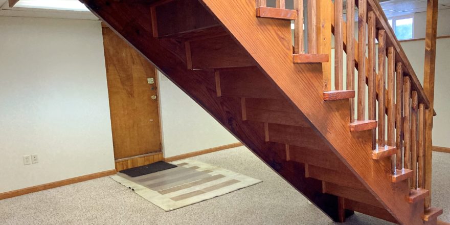 Basement den with carpet and wooden stairwell in the middle of the room