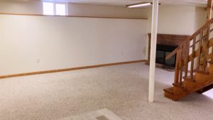 Basement den with fireplace and wood staircase in the middle of the room