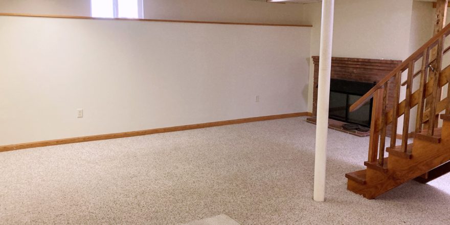 Basement den with fireplace and wood staircase in the middle of the room