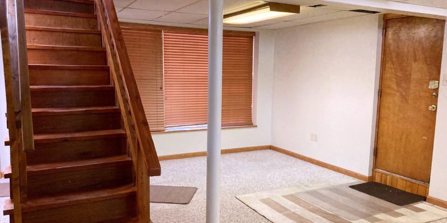 Basement den with carpet and wooden stairwell in the middle of the room