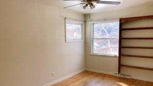 Unfurnished bedroom with wood floors, ceiling fan, and wall-mounted bookshelf