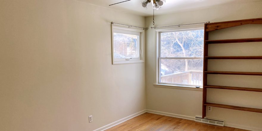 Unfurnished bedroom with wood floors, ceiling fan, and wall-mounted bookshelf