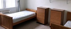 Carpeted bedroom with two twin beds, shelving, and wooden chests of drawers