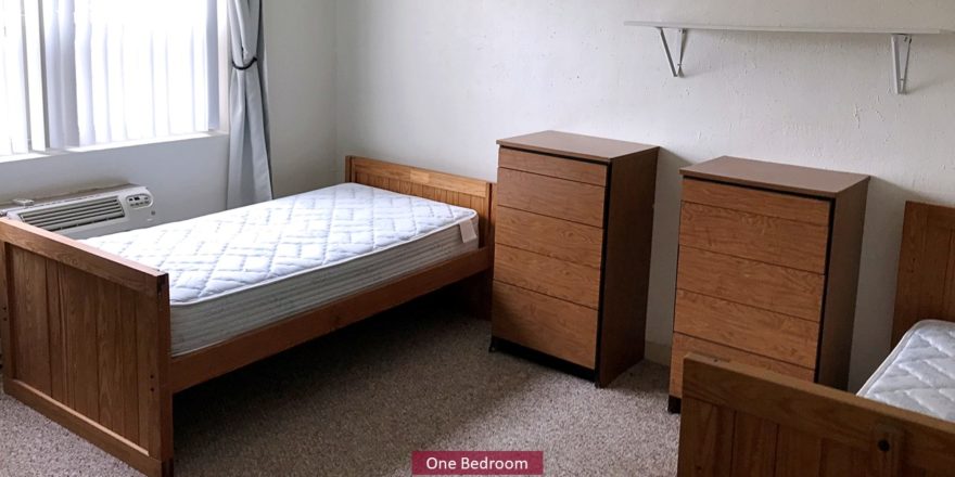 Carpeted bedroom with two twin beds, shelving, and wooden chests of drawers