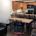 Kitchen with black appliances, wood-tone cabinets and bar seating. Living Room with couch and dining table.