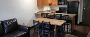 Kitchen with black appliances, wood-tone cabinets and bar seating. Living Room with couch and dining table.