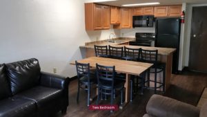 Kitchen with black appliances, wood-tone cabinets and bar seating. Living Room with couch and dining table.