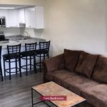 Kitchen with stainless steel appliances, white cabinets and bar seating. Living Room with couch and coffee table.