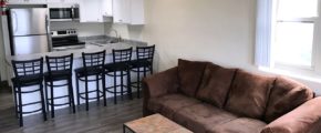 Kitchen with stainless steel appliances, white cabinets and bar seating. Living Room with couch and coffee table.