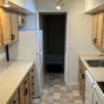 a narrow kitchen with wooden cabinets and white appliances