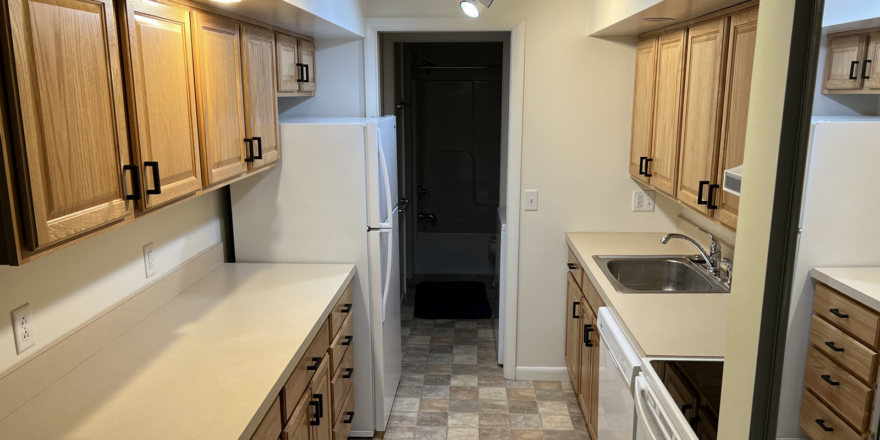 a narrow kitchen with wooden cabinets and white appliances