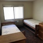 Carpeted bedroom with 2 beds, 2 dressers, window, and AC unit
