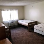 Carpeted bedroom with 3 beds, 2 dressers, window, and AC unit