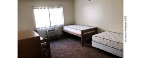 Carpeted bedroom with 3 beds, 2 dressers, window, and AC unit
