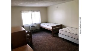 Carpeted bedroom with 3 beds, 2 dressers, window, and AC unit