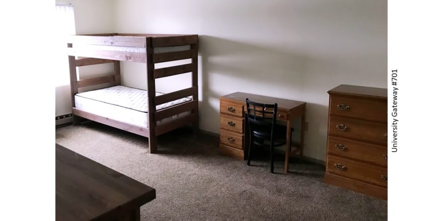 Carpeted bedroom with bunk bed, desk with chair, and two dressers