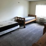 Carpeted bedroom with three beds, two dressers, AC unit, and window
