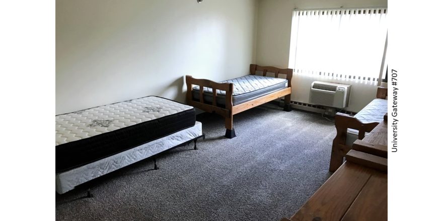 Carpeted bedroom with three beds, two dressers, AC unit, and window