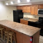 Kitchen with wood-tone cabinets, brown countertop, barstools, and black appliances