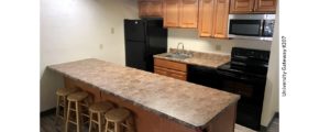 Kitchen with wood-tone cabinets, brown countertop, barstools, and black appliances