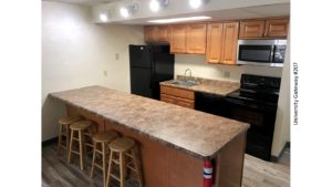 Kitchen with wood-tone cabinets, brown countertop, barstools, and black appliances