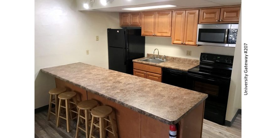 Kitchen with wood-tone cabinets, brown countertop, barstools, and black appliances