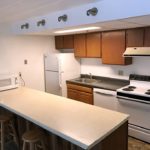 Kitchen with wood-tone cabinets, beige and gray counter tops, barstools, and white appliances