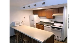 Kitchen with wood-tone cabinets, beige and gray counter tops, barstools, and white appliances