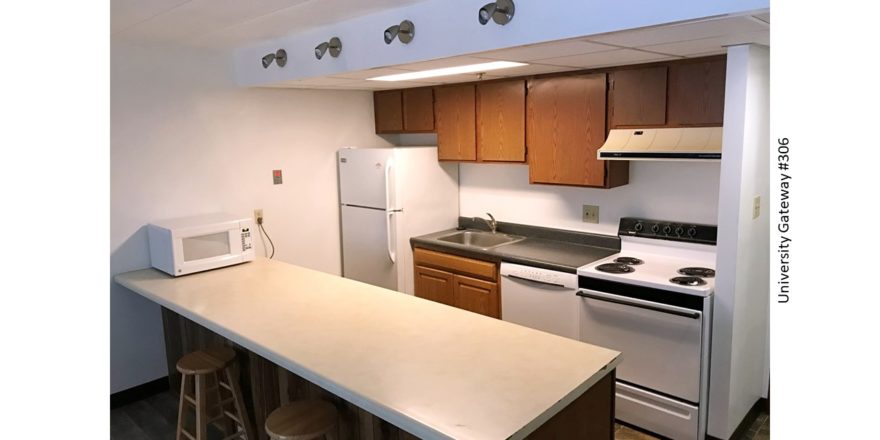 Kitchen with wood-tone cabinets, beige and gray counter tops, barstools, and white appliances