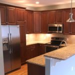 Kitchen with dark wood cabinets, wood-style flooring, stainless steel appliances, stone countertops