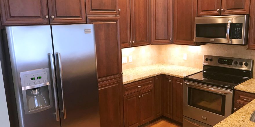 Kitchen with dark wood cabinets, wood-style flooring, stainless steel appliances, stone countertops