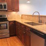 Kitchen with dark wood cabinets, wood-style flooring, stainless steel appliances, stone countertops