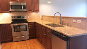 Kitchen with dark wood cabinets, wood-style flooring, stainless steel appliances, stone countertops