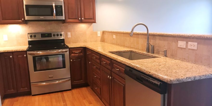 Kitchen with dark wood cabinets, wood-style flooring, stainless steel appliances, stone countertops