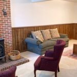 Carpeted basement den with wood wainscot, brick hearth, wood burning fireplace, and furniture