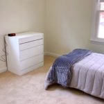 Carpeted bedroom with twin bed, dresser, windows, and clock