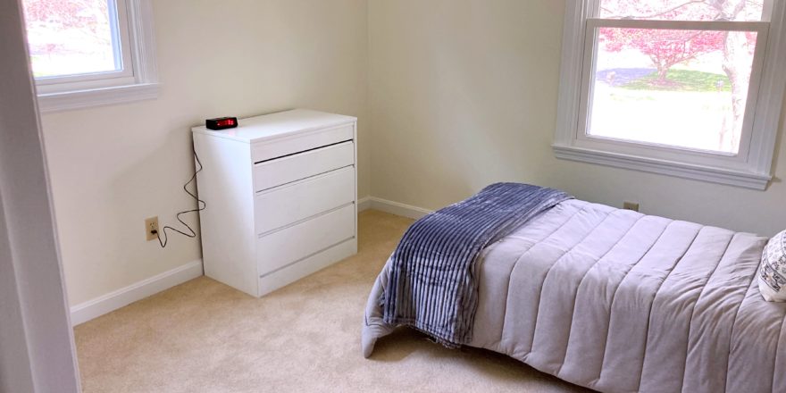 Carpeted bedroom with twin bed, dresser, windows, and clock