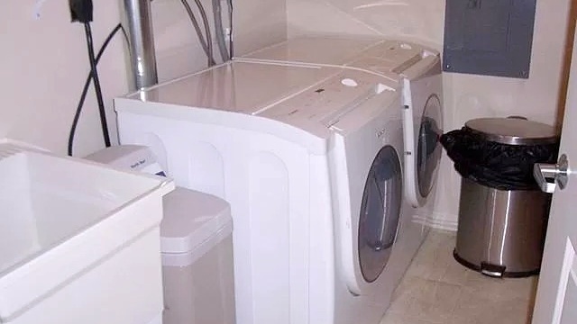 Laundry room with side-by-side front load washer and dryer, laundry sink, and trashcan