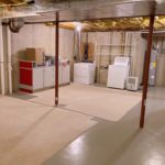 Unfinished basement with carpet squares, cabinets, and laundry machines
