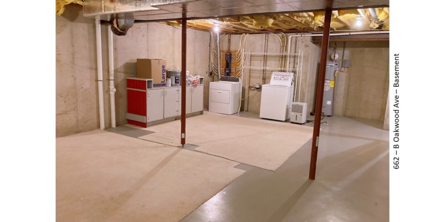 Unfinished basement with carpet squares, cabinets, and laundry machines