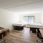 Bedroom with wood-style laminate flooring, 2 desks with chairs, 4 dressers, and 2 full beds