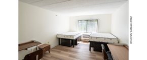 Bedroom with wood-style laminate flooring, 2 desks with chairs, 4 dressers, and 2 full beds