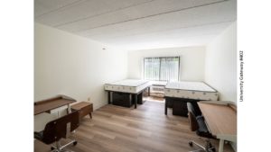 Bedroom with wood-style laminate flooring, 2 desks with chairs, 4 dressers, and 2 full beds