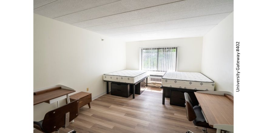 Bedroom with wood-style laminate flooring, 2 desks with chairs, 4 dressers, and 2 full beds