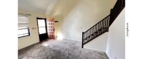 Carpeted, unfurnished living room with staircase, large windows and cathedral ceiling