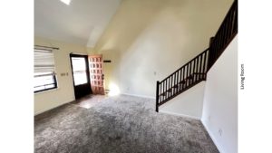 Carpeted, unfurnished living room with staircase, large windows and cathedral ceiling