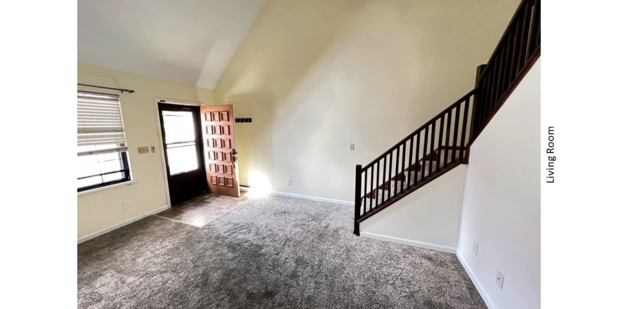 Carpeted, unfurnished living room with staircase, large windows and cathedral ceiling