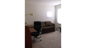 Bedroom set up as an office with a love seat, desk chair, and desk