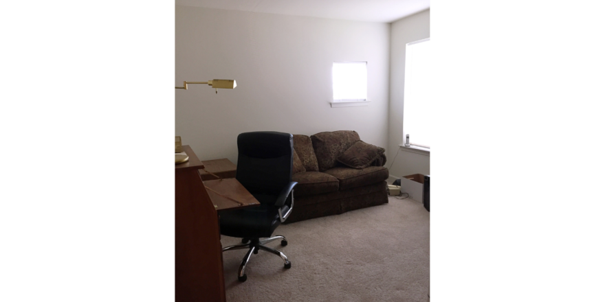 Bedroom set up as an office with a love seat, desk chair, and desk